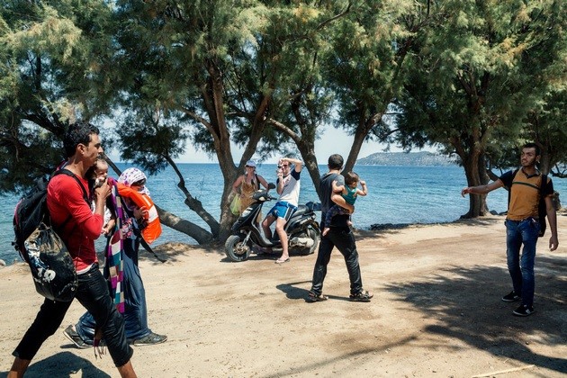 2015. Lesbos. Grčka. Dvoje turista fotografiraju sirijsku obitelj koja se upravo iskrcala na Eftalou na sjeveru grčkog otoka Lezbos.