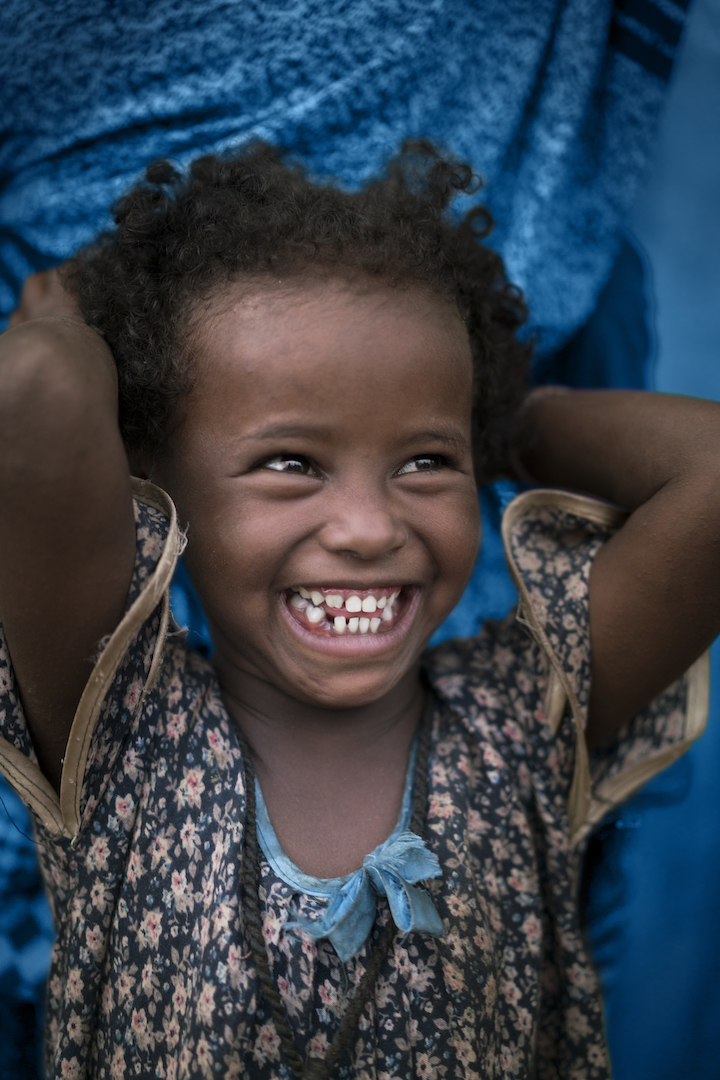 [TREATED PHOTO. RELEASE OBTAINED] On 10 October 2016, Amal Mohammed stands in front of her mother wearing a black and peach flowered dress. Amal smiles for the camera with her arms up behind her head. She has soft curly hair and is missing a tooth in her huge smile. She lives in a village near the town of Jigjiga, Ethiopia where UNICEF monitor Child Health and Early Childhood Development. UNICEF's initiatives represented here are Child Survival and Development, health, and strength of the girl child. As part of the UNICEF Brand strategy and re-positioning initiated in 2016, this signature photograph was taken to showcase children being children, as direct or indirect beneficiaries of UNICEF’s work around the world. This photo is designed to be used for both specific messaging around certain programmatic or thematic areas and/or general and emotional use under the modular brand device “for every child, ...”. This photograph is for editorial use & fundraising use by UNICEF in editorial contexts in digital or traditional platforms such as UNICEF publications and global, COs, ROs and National Committee digital or traditional platforms to advocate, raise awareness and fundraise in digital campaigns and appeals. The United Nations Children’s Fund (UNICEF) is one of the most trusted names in international development and humanitarian action, with a presence in over 190 countries and territories. That trust has been earned over the course of over 70 years by delivering and renewing a promise made to promote the rights and well-being of every child, everywhere. UNICEF’s brand is a strategic asset that improves the organization’s ability to fulfil its mission. It builds goodwill among UNICEF supporters, improves recognition among our audiences and strengthens our reputation with partners, aiding in the building of three key brand attributes - trust. respect and high visibility. [TREATED PHOTO] may be used for editorial use & fundraising use by UNICEF in e